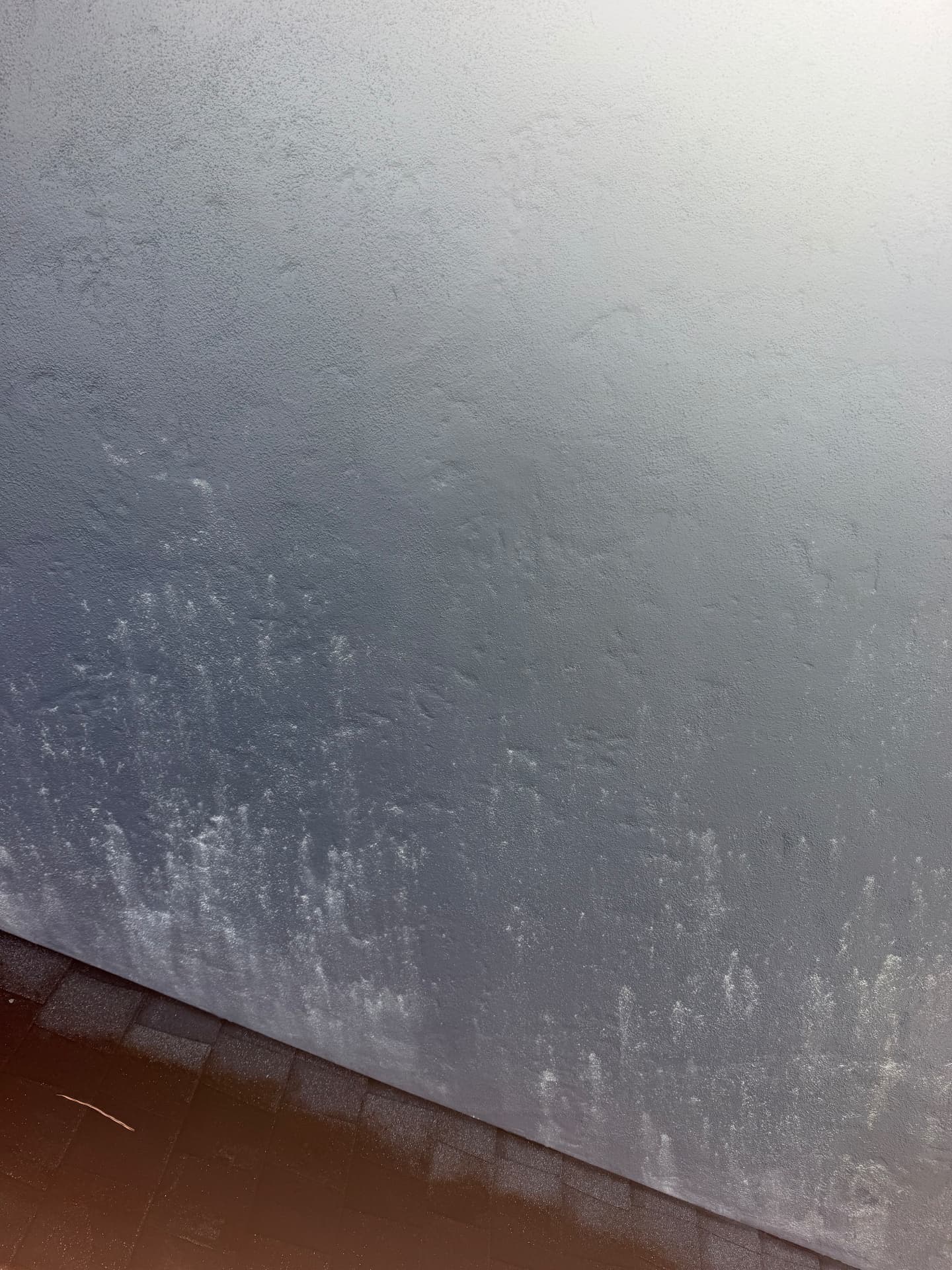 Painted stucco wall above a shingle roofline covered in chalky white mineral splash marks before house soft washing in Orlando, FL